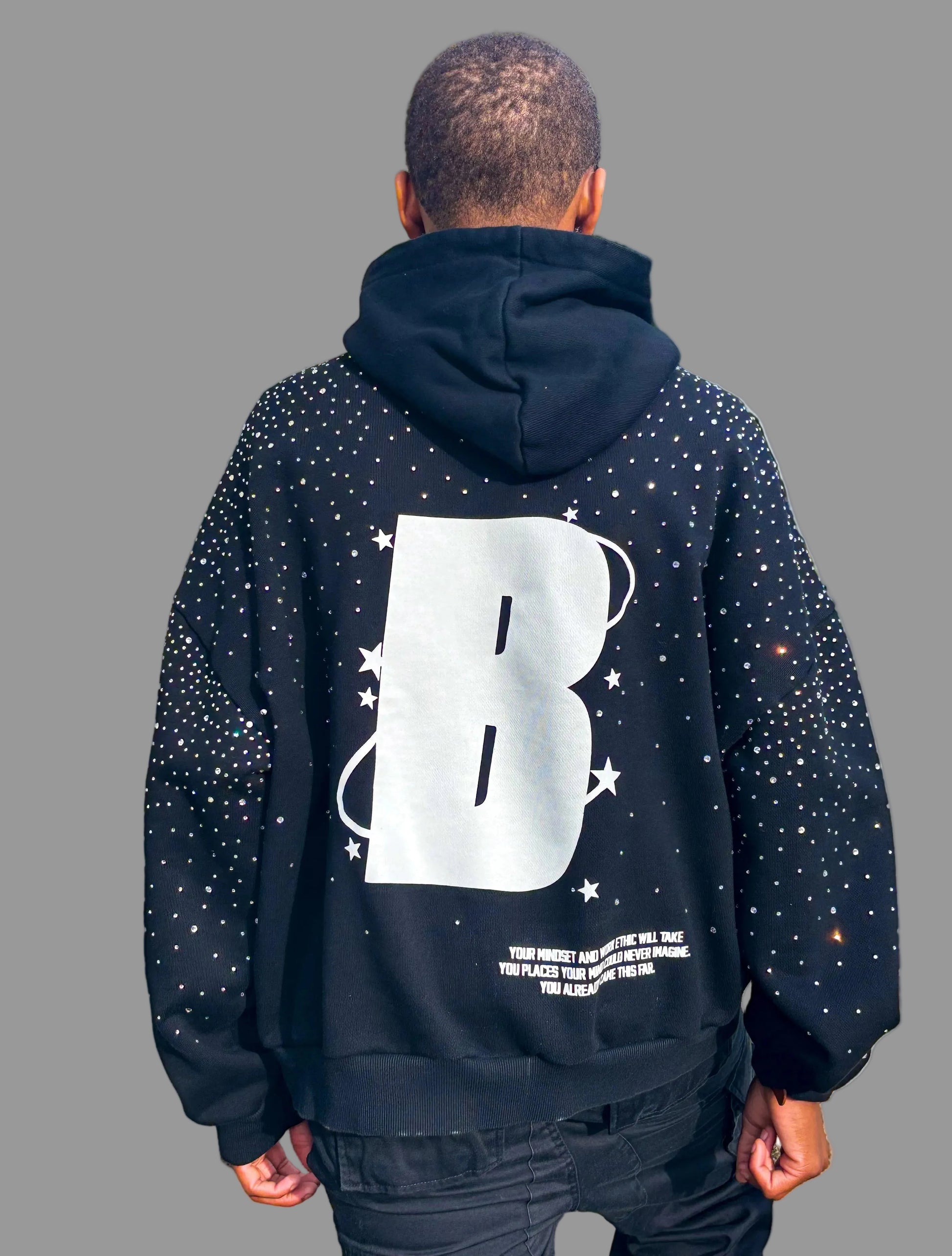 Person wearing a black hoodie with a large white letter 'B' on the back, standing outdoors.
