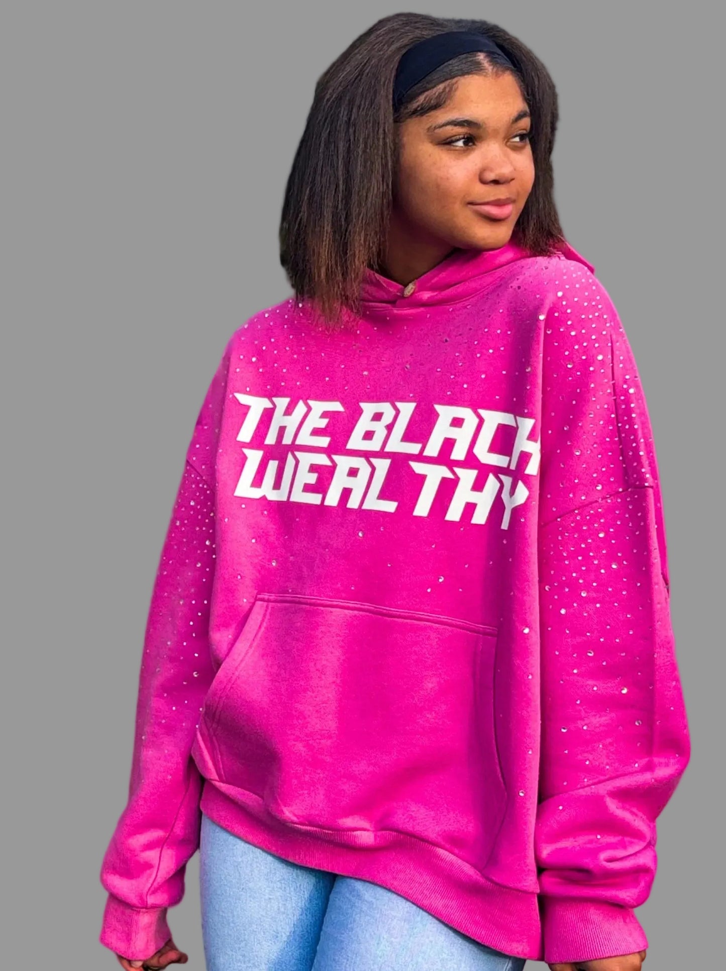 Person wearing a pink hoodie with 'THE BLACK WEALTHY' text, standing outdoors.