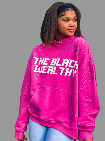 Person wearing a pink hoodie with 'THE BLACK WEALTHY' text, standing outdoors.