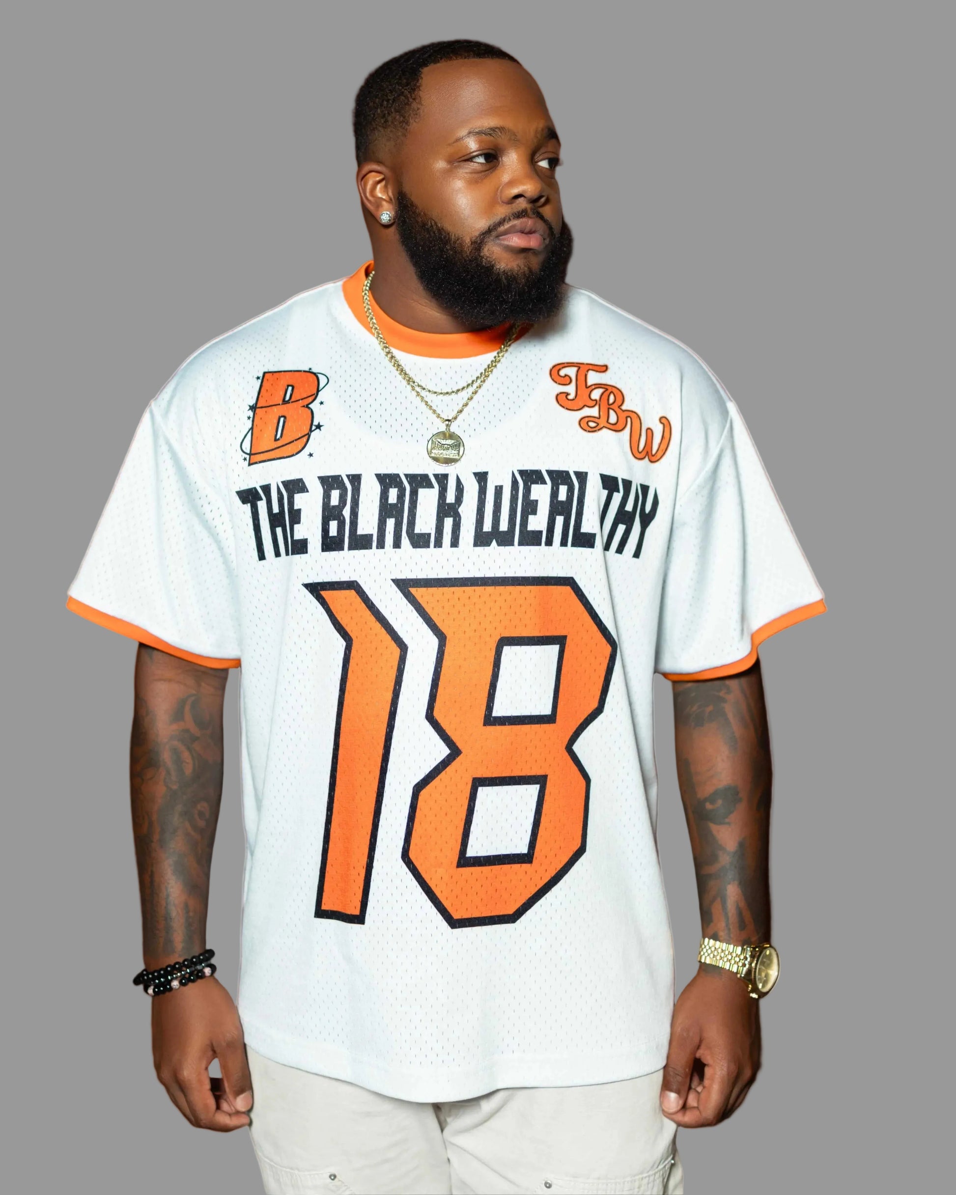 Man wearing a white sports jersey with orange and black text and numbers, standing against a red brick wall.